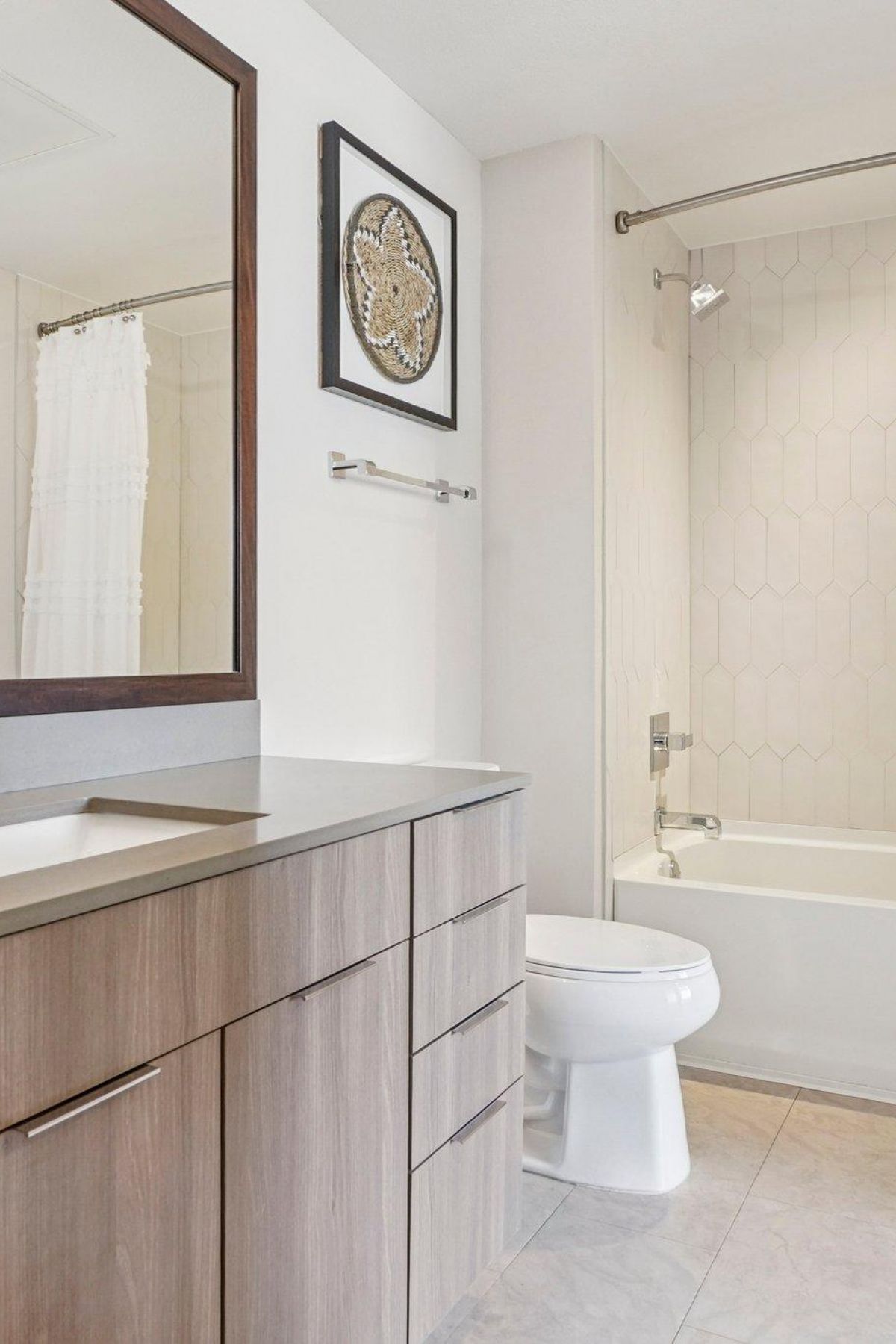 Ascent modern bathroom with wood cabinets, a large mirror, toilet, and a bathtub with a white shower curtain.