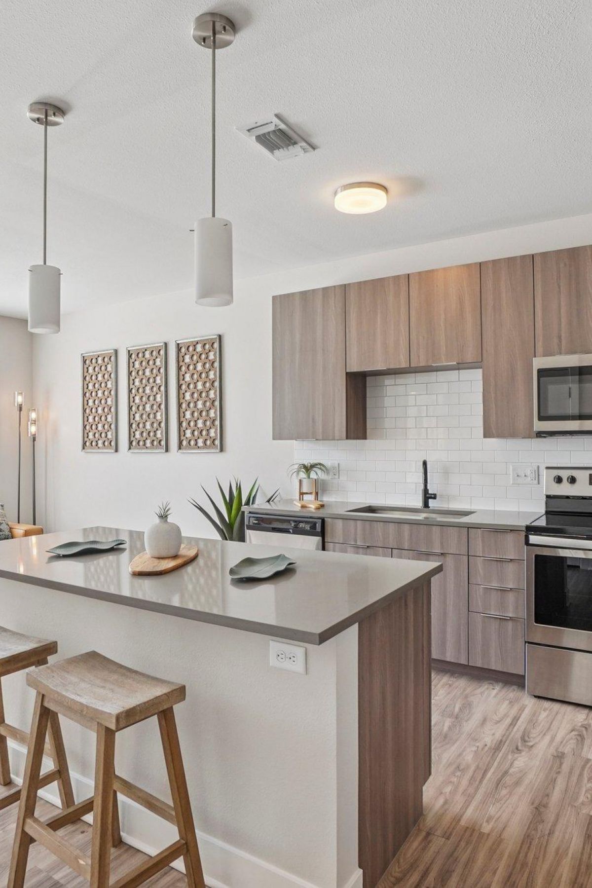 Ascent modern kitchen with wood cabinets, island with stools, stainless steel appliances, and bright living area.